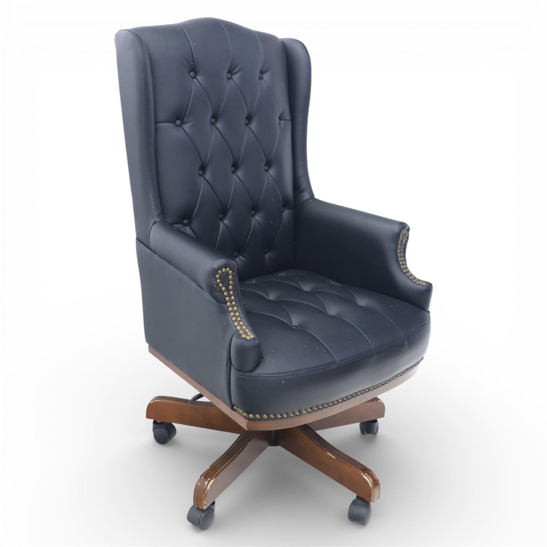 Chesterfield style desk chair upholstered in black, brass studded trim with tall button backed seat, with faux wooden base raised upon castors