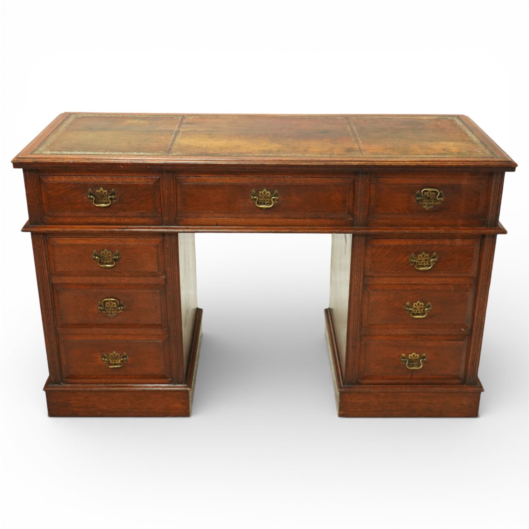 Late Victorian oak nine drawer desk, the rectangular top inset with a tooled leather writing surface bordered in gilt, above three frieze drawers and two pedestal cupboards each fitted with three graduated drawers, all with brass swan neck handles, raised on plinth bases