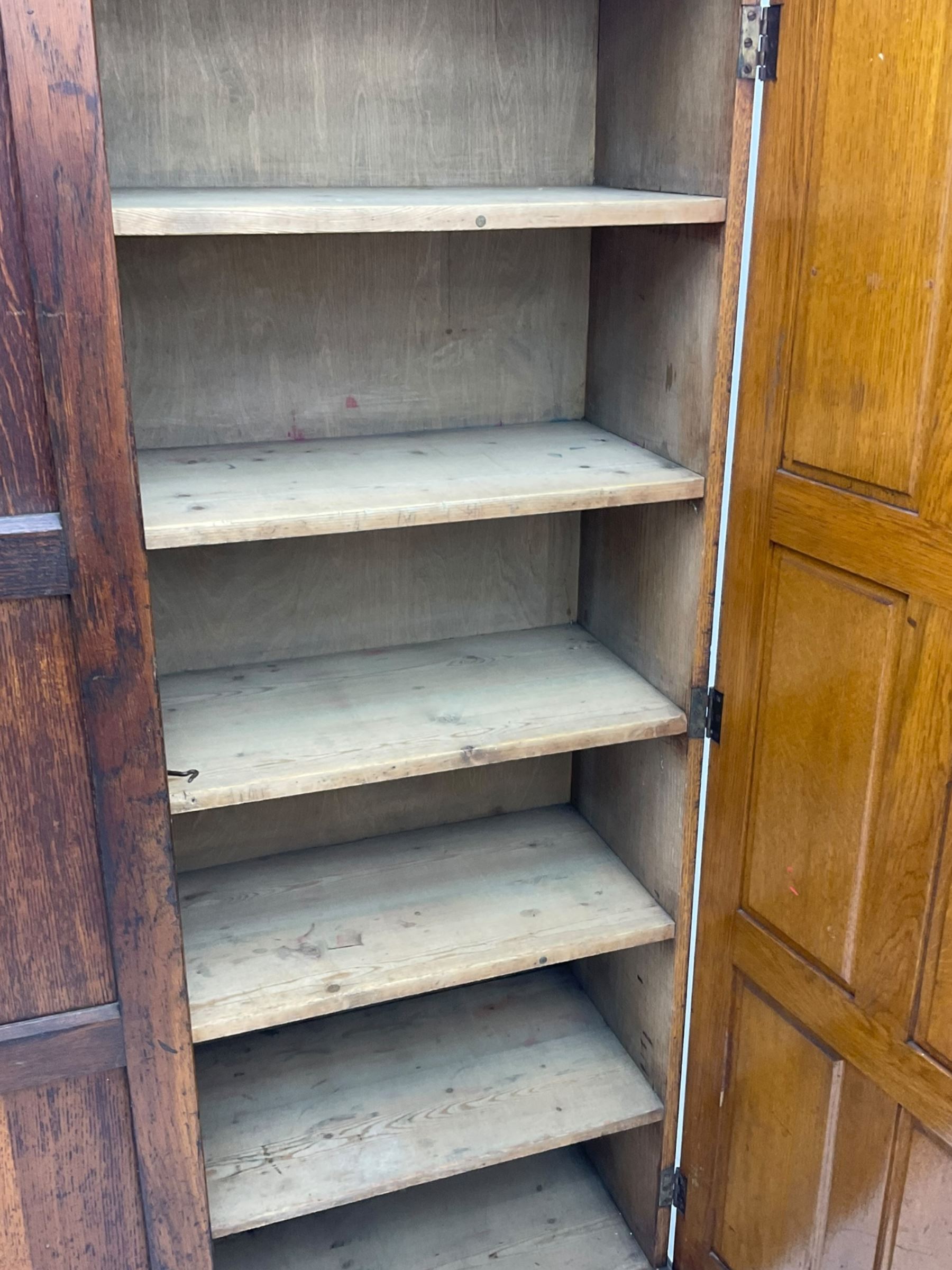 The North of England School Furnishing Company Limited Darlington - early 20th century oak school cupboard, projecting moulded cornice over two panelled doors, fitted with shelves, on chamfered plinth base 