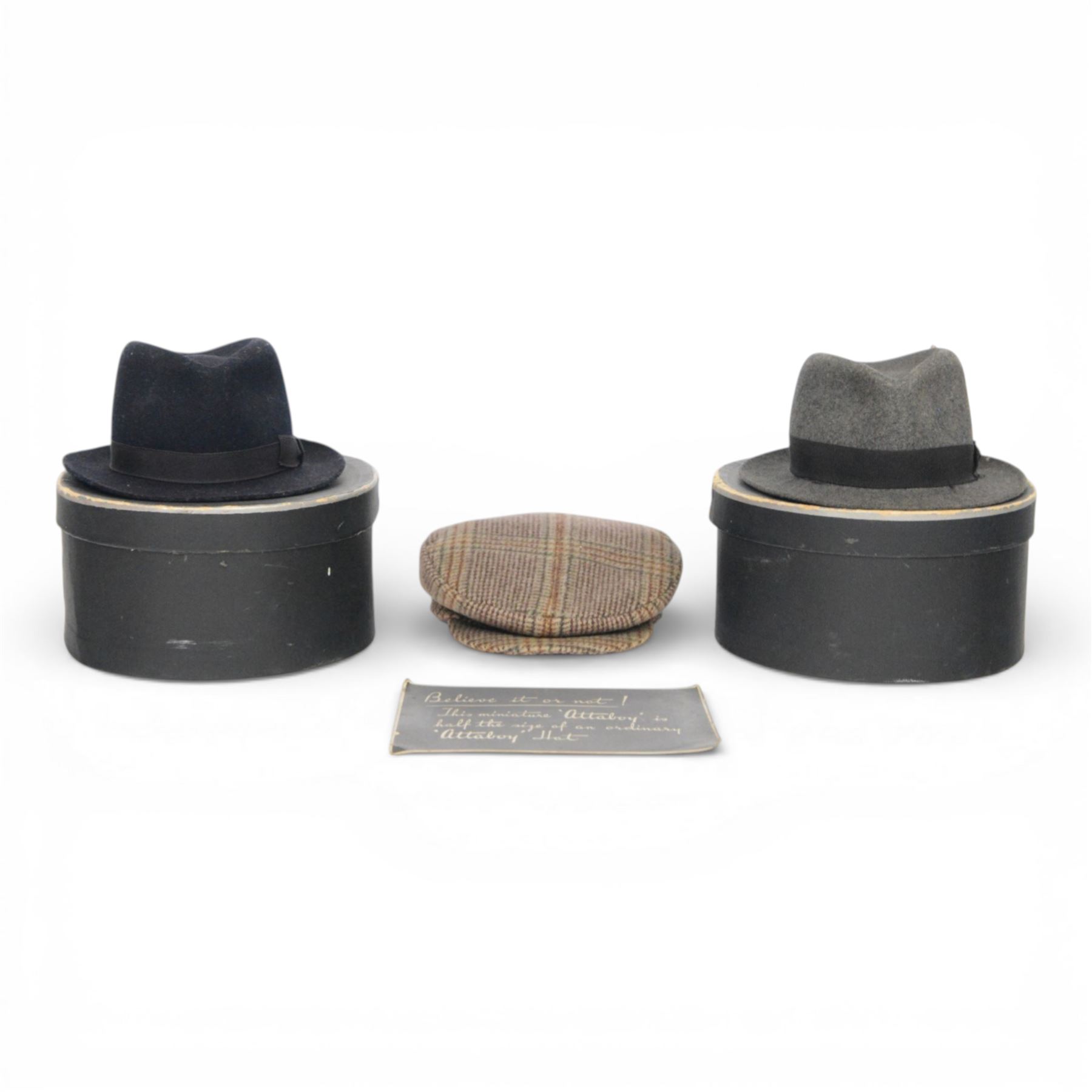 Two Attaboy tradesman or miniature trilbies, in black miniature hat boxes, one with a certificate 'Believe it or not! this miniature 'Attaboy' is half the size of an ordinary 'Attaboy' hat' together with a miniature flat cap, trilby H7cm     