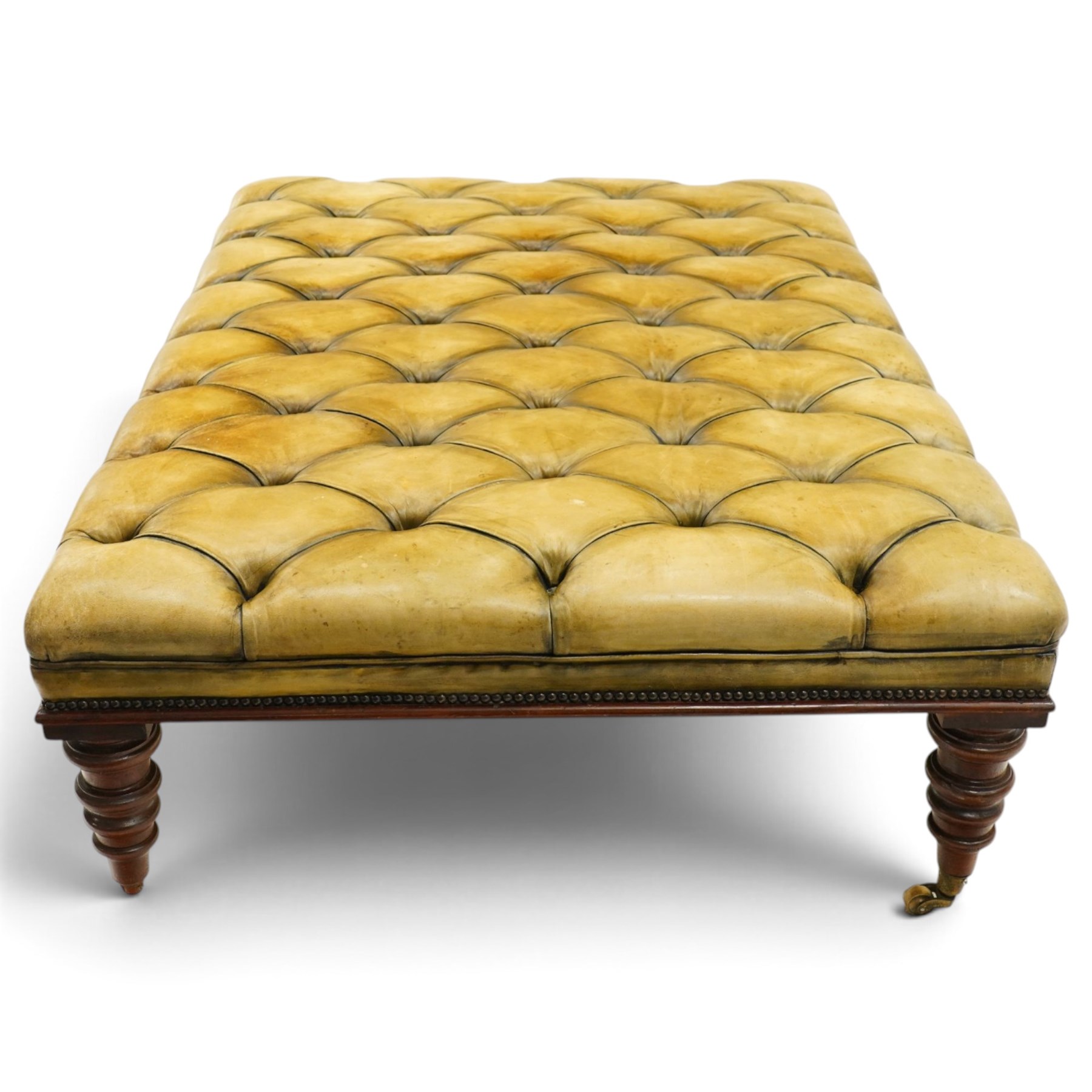 Georgian design footstool of generous proportions, the large rectangular seat upholstered in olive green buttoned leather, raised on heavily turned supports with brass castors