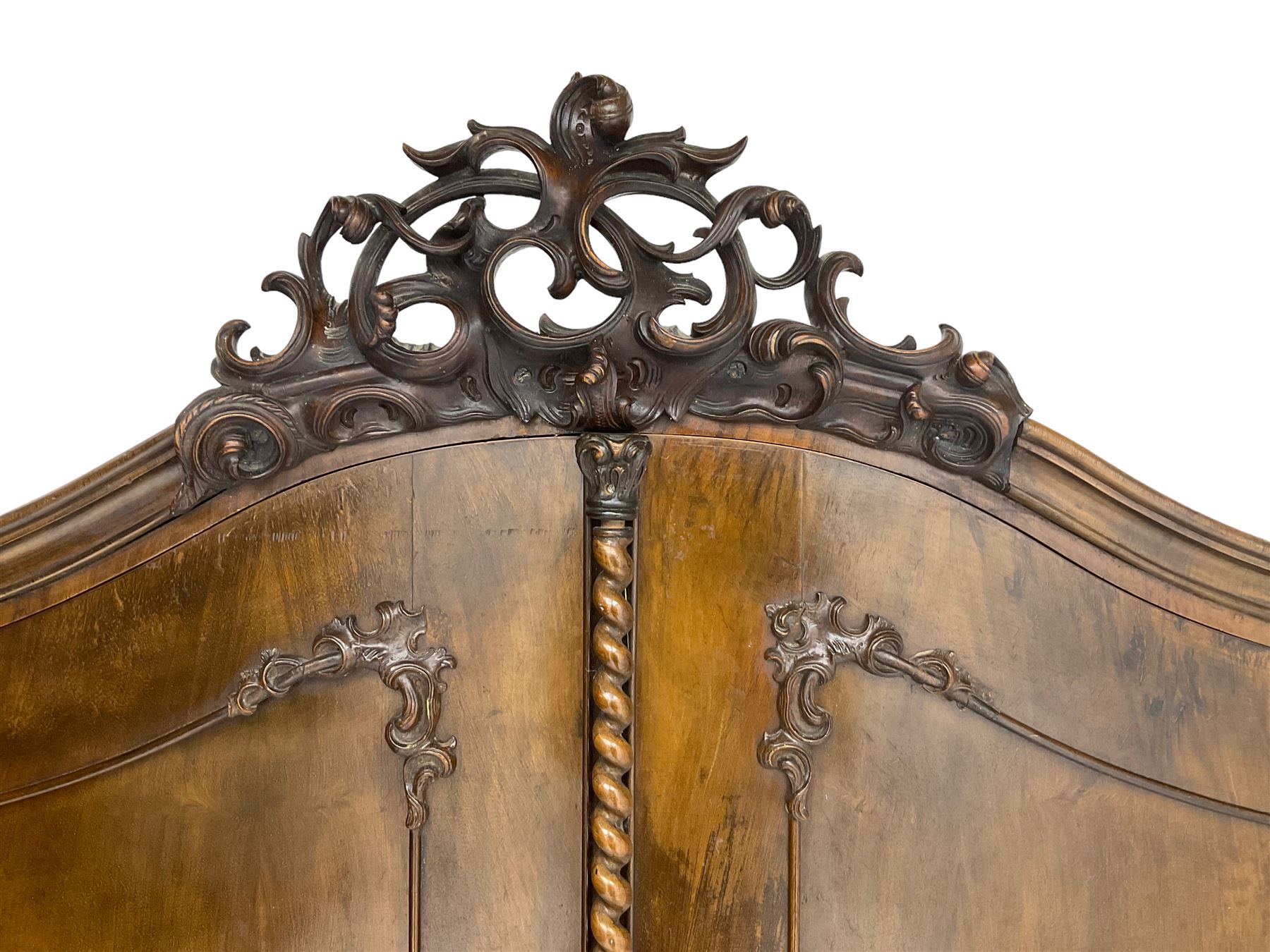 Early 20th century Italian walnut armoire wardrobe, the pierced and scrolling pediment carved with acanthus leaf detail, flanked by two scrolling cartouche with matching corbels below, the two panelled doors with applied carved rinceaux slips, with a central spiral turned upright, enclosing single shelf and hooks, raised on scroll feet
