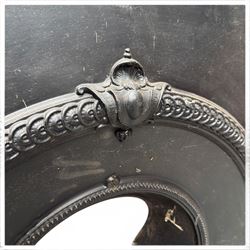 Late Victorian black-painted cast iron fireplace, the arched surround with anthemion cartouche and guilloche-moulded border, enclosing a bow-front fire basket with finialled standards, railed front and leaf-cast apron, with sheet-metal backplate