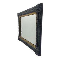 Small black painted and gilt wall mirror, in ornate frame decorated with floral cartouches, plain mirror plate