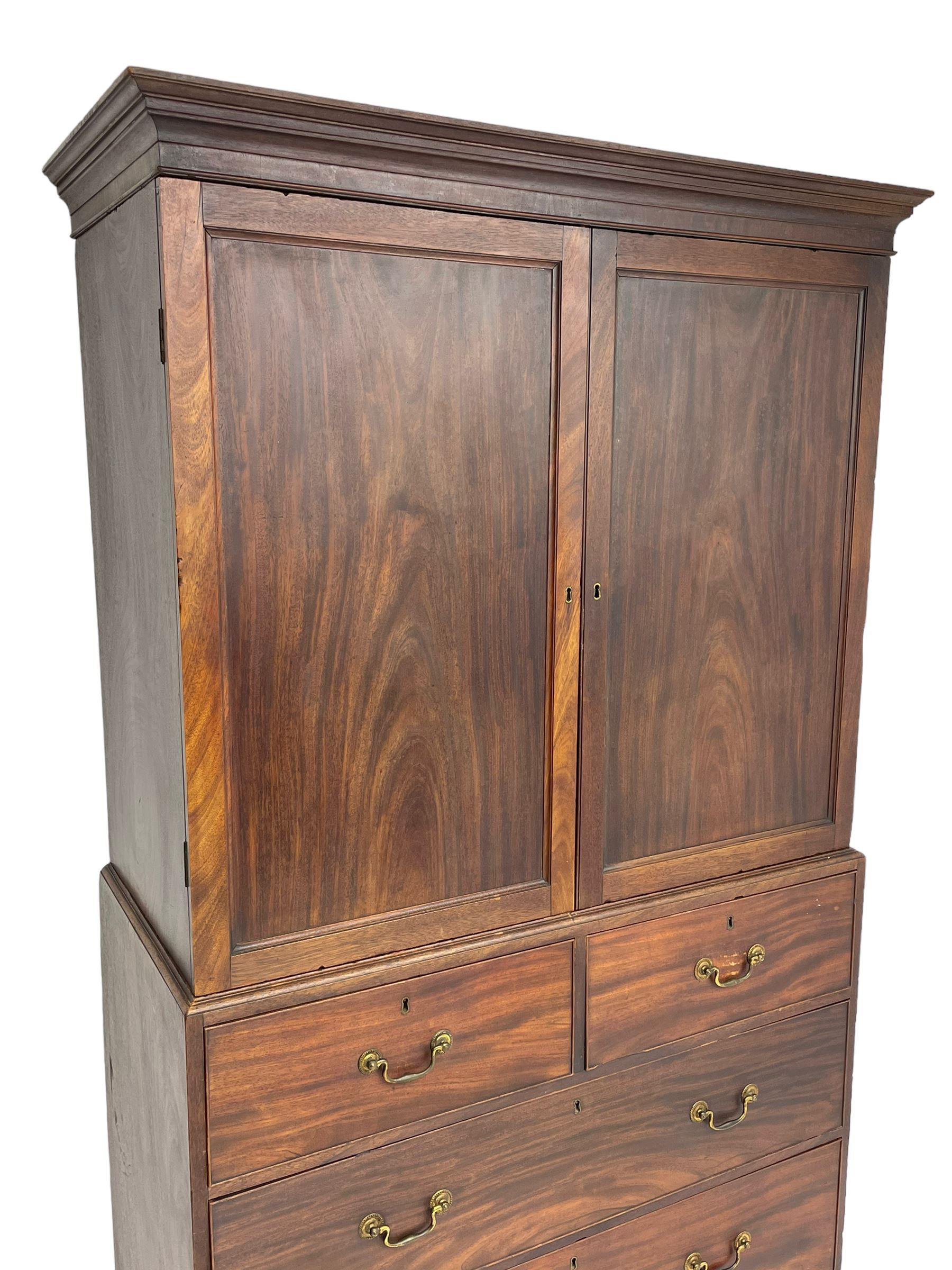 George III mahogany Gentleman's linen press, the projecting cornice over two panelled cupboard doors enclosing three sliding trays, the base fitted with two short over three long graduating cock-beaded drawers, lower moulded edge over bracket feet