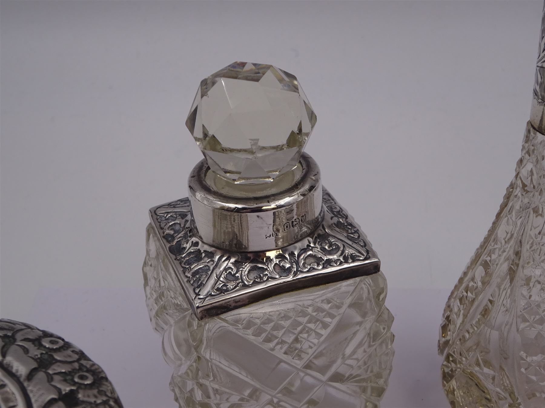 Two silver mounted dressing table jars, one in the form of a heart, both with embossed silver covers and cut glass bodies, hallmarked, together with two smaller examples, one set with mother of pearl, three silver mounted glass scent bottles, including an example with prunus blossom decoration, stamped Sterling, tallest bottle H17cm