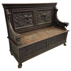 19th century oak hall bench, dentil cresting rail over moulded frame with panelled back carved with fire-breathing mythical beasts and central acanthus leaf motif, scroll carved down-sweeping arms carved with grotesque masks with scrolled foliage and shells, hinged box seat carved with scrolling foliage over panelled front with further carved foliage decoration, on paw carved front feet 