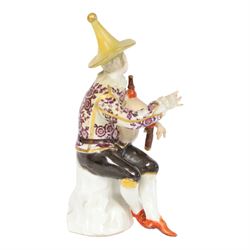 Mid 18th century Meissen figure, modelled as a harlequin playing bagpipes, circa 1745, possibly modelled by J.F.Eberlein after earlier models by J.J.Kändler, wearing a gilt edged tunic painted with flowers, black breeches with rosettes at the knees, red shoes and conical yellow hat, seated upon a rock, with traces of blue crossed swords mark beneath, H14cm