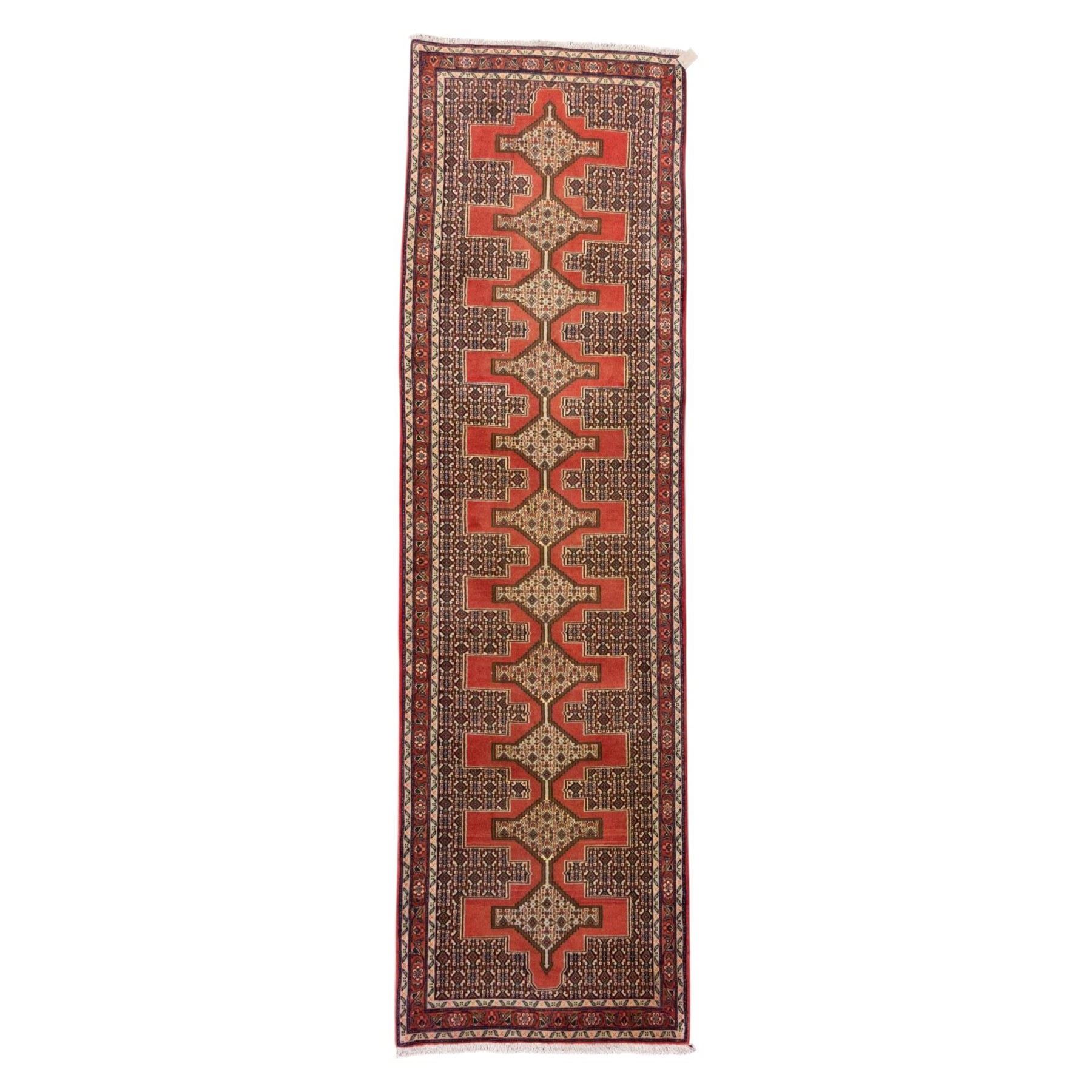 North West Persian Senneh hand-knotted runner, decorated with a continuous series of stepped and hooked geometric medallions against a madder red ground, enclosing herati style and small geometric floral motifs, framed by a principal border and flanked by multiple narrow guard stripes, with cotton fringe ends 