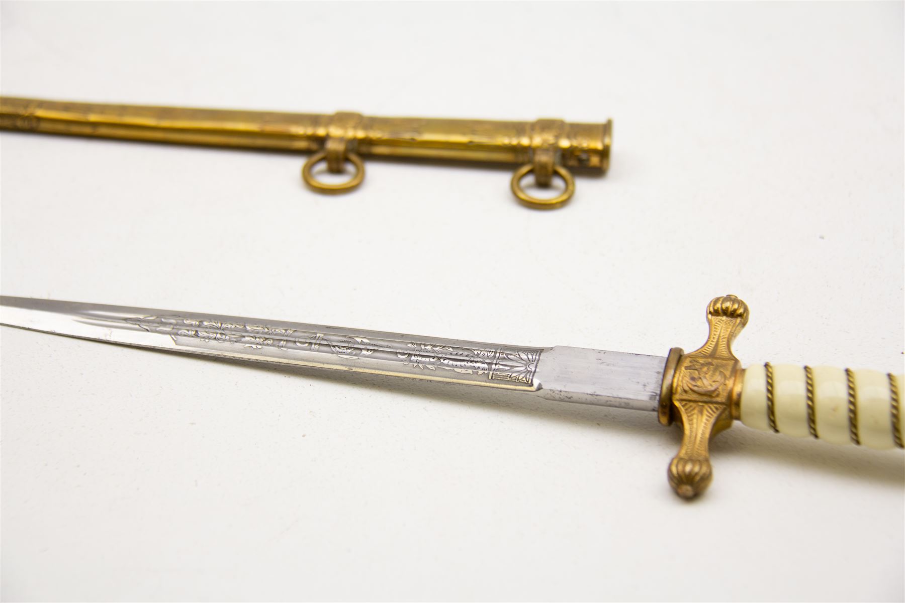 WWII period German Kriegsmarine navel officers dress dagger by Carl Eickhorn, Solingen, with gilded pommel and cross guard with press stud release button, white celluloid grip with wire binding, housed in its original brass scabbard with two hanging rings, the etched double edged blade with Carl Eickhorn, Solingen makers trademark to the base, L39cm