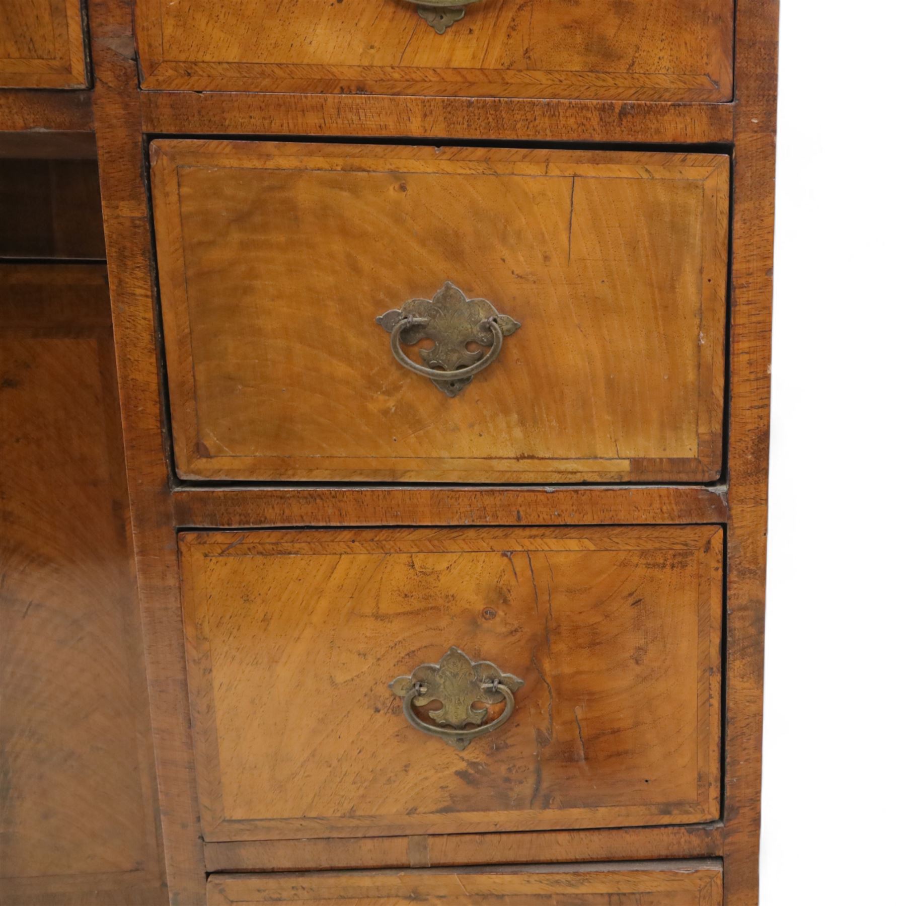 Early 20th-century Georgian-style walnut kneehole desk, the rectangular top with feather cross-banded border, above an arrangement of eight short drawers flanking a central cupboard door, fitted with brass backplate handles, raised on bracket feet