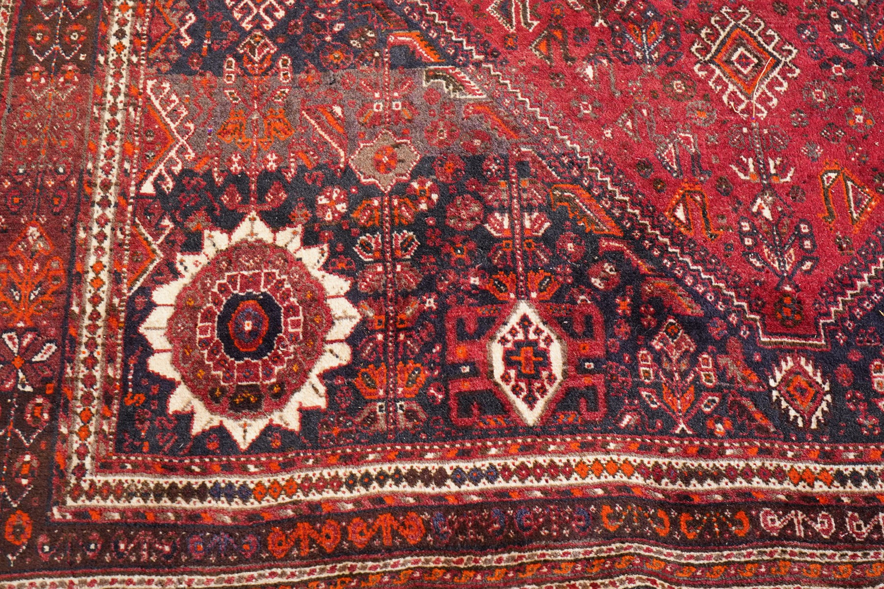 Large Persian Shiraz crimson ground carpet, the busy field decorated with a geometric pole medallion surrounded by stylised plant motifs with contrasting indigo spandrels and geometric-woven guard bands