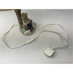 Nao table lamp modelled as a boy playing the flute upon logs with two recumbent sheep at his feet, the stem modelled as a tree trunk, with fabric shade, with printed mark beneath, H46cm