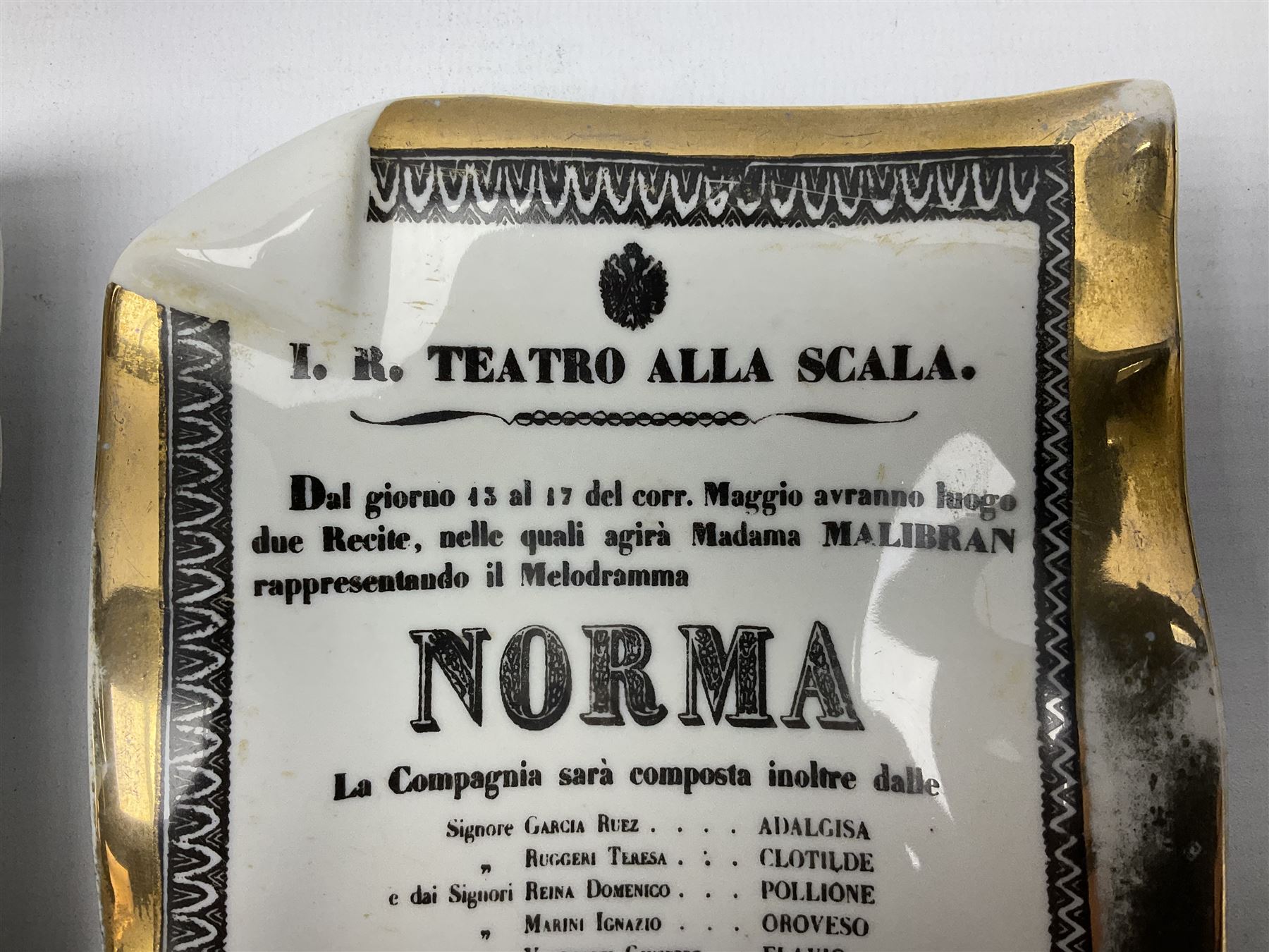 Two Fornasetti rectangular operatic posters ashtrays 'Norma' and 'Iris' decorated with black and white text with a gilt border edge, with printed mark beneath, H16cm