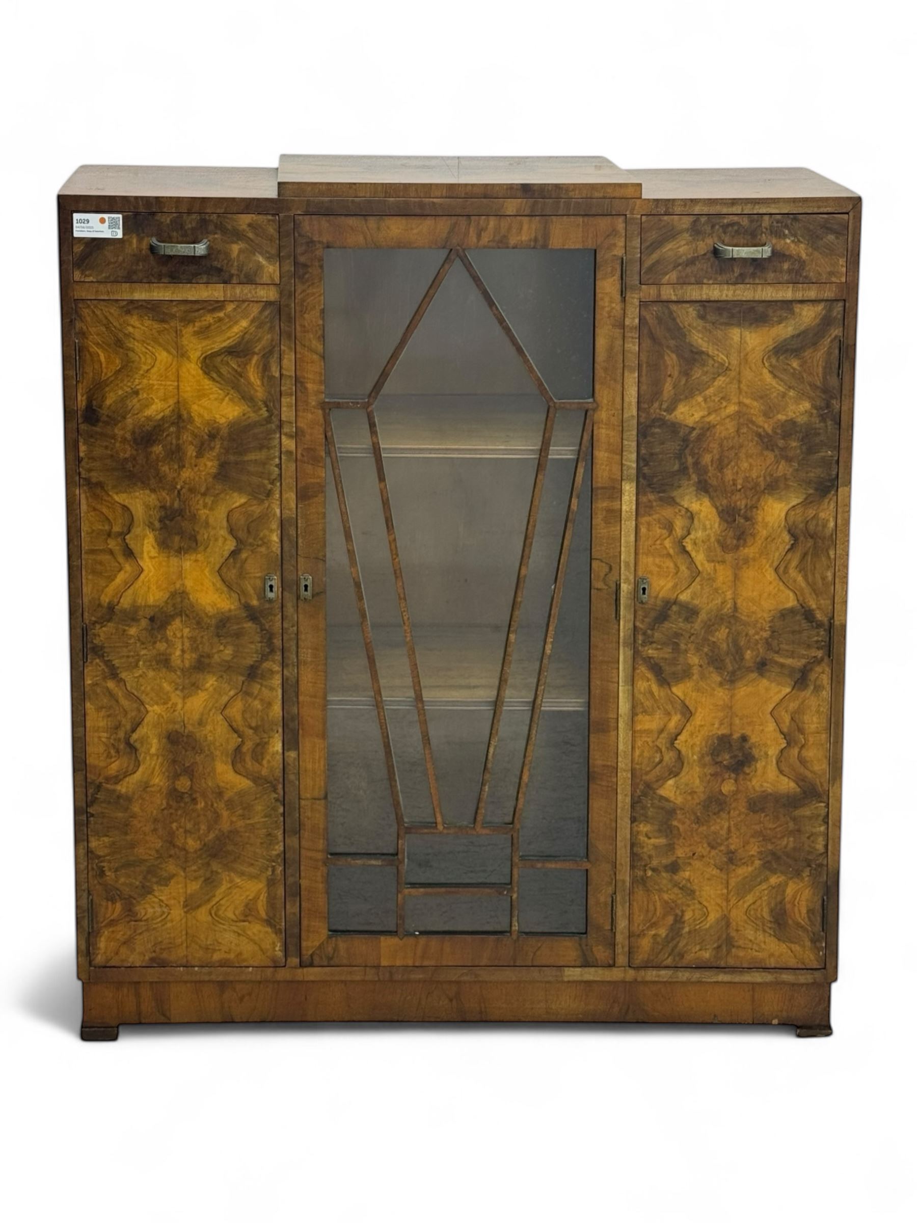 Art Deco burr walnut drinks cabinet, geometric central glazed astragal door enclosing two fixed shelves, flanked by symmetrical bookmatched veneered cupboards with drawers above 