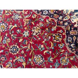 Pair of Persian wool rugs, each with rich red ground, one centred with a diamond-shaped medallion and navy spandrels within a floral field, the other with radiating floral medallion and scrolling foliate motifs, both enclosed by multiple borders with palmette and flowerhead designs, from the region of Kashan 291x376, 299 x 378 