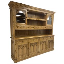 Ecclesiastical Gothic design waxed pine 8’ dresser, projecting cornice over two display cabinets, central shelf and ten small drawers, rectangular moulded top over four drawers and four cupboards, the doors with Gothic design arched panels carved with flower heads and foliage, on plinth base