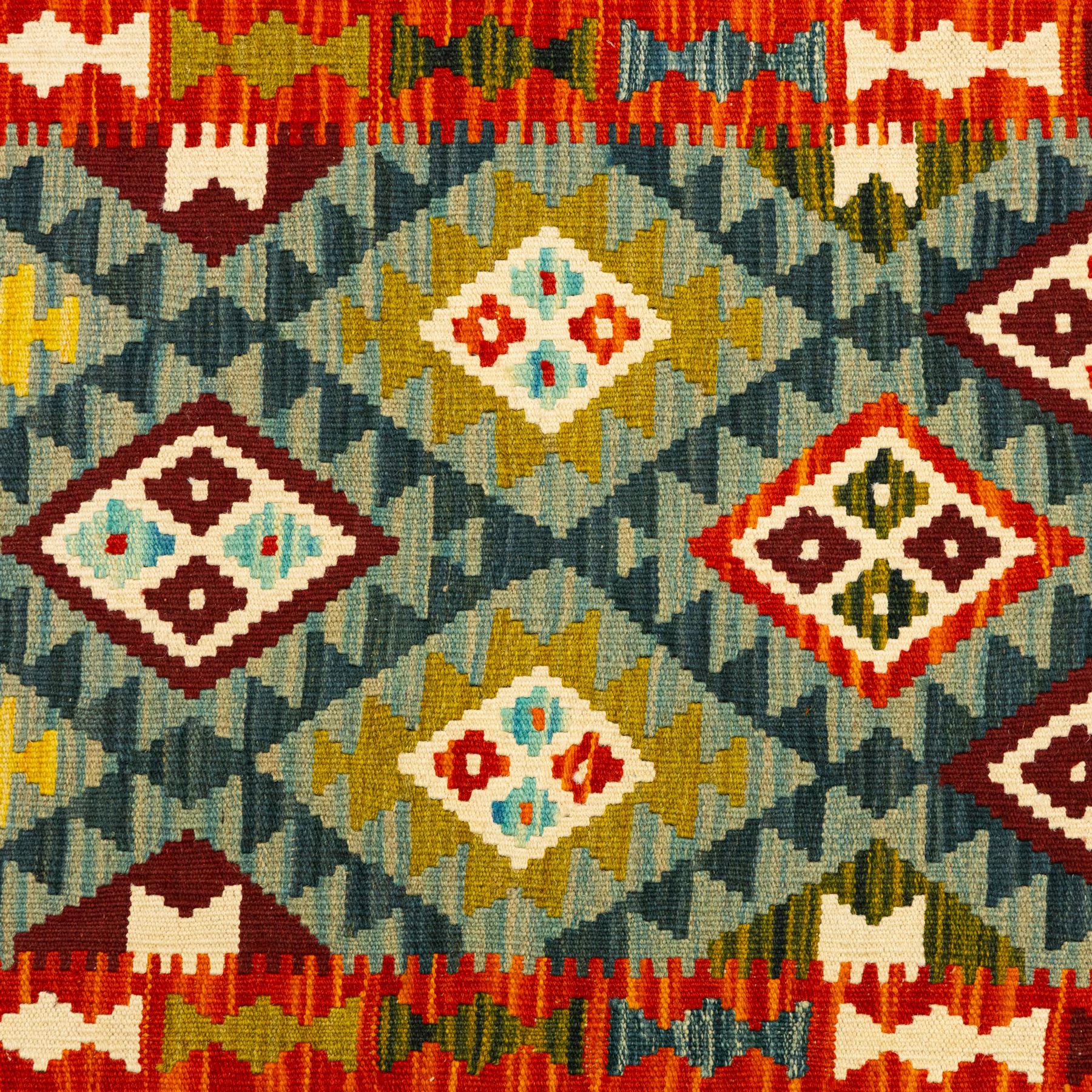 Afghan Maimana kilim flatweave runner, central field features a large bold nested diamond motifs and stylized geometric lozenge patterns on crimson, olive purple, blue, and green tone ground, border stripe in teal ground, and fringe