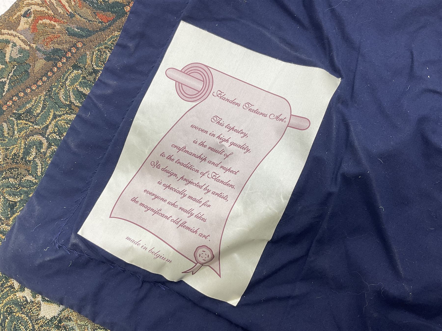 Three tapestries comprising 20th century wool tapestry panel of a medieval nobleman upon a horse with a castle in the distance, together with a smaller tapestry depicting The English Coat of Arms, both hung on rails, and further depicting village scene, largest approx 132cm x 95cm