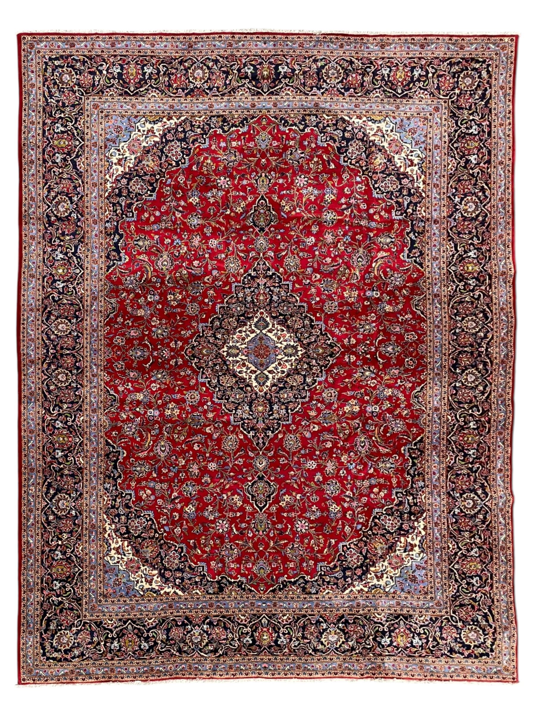 Persian Kashan crimson ground carpet, floral pattern indigo ground central medallion and matching spandrels, the field decorated densely with scrolling foliate patterns and floral motifs, the main border decorated with scrolling branches and palmettes, within floral pattern guard stripes