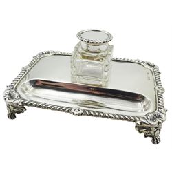Early 20th century silver desk stand, of rectangular form with gadrooned rim with shell detail to corners, and recessed pen tray before a removable clear glass inkwell of square form with silver mounted cover, the stand upon four foliate mounted paw feet, hallmarked E S Barnsley & Co, Birmingham 1913, tray W17cm, approximate weighable silver 8.35 ozt (260 grams)