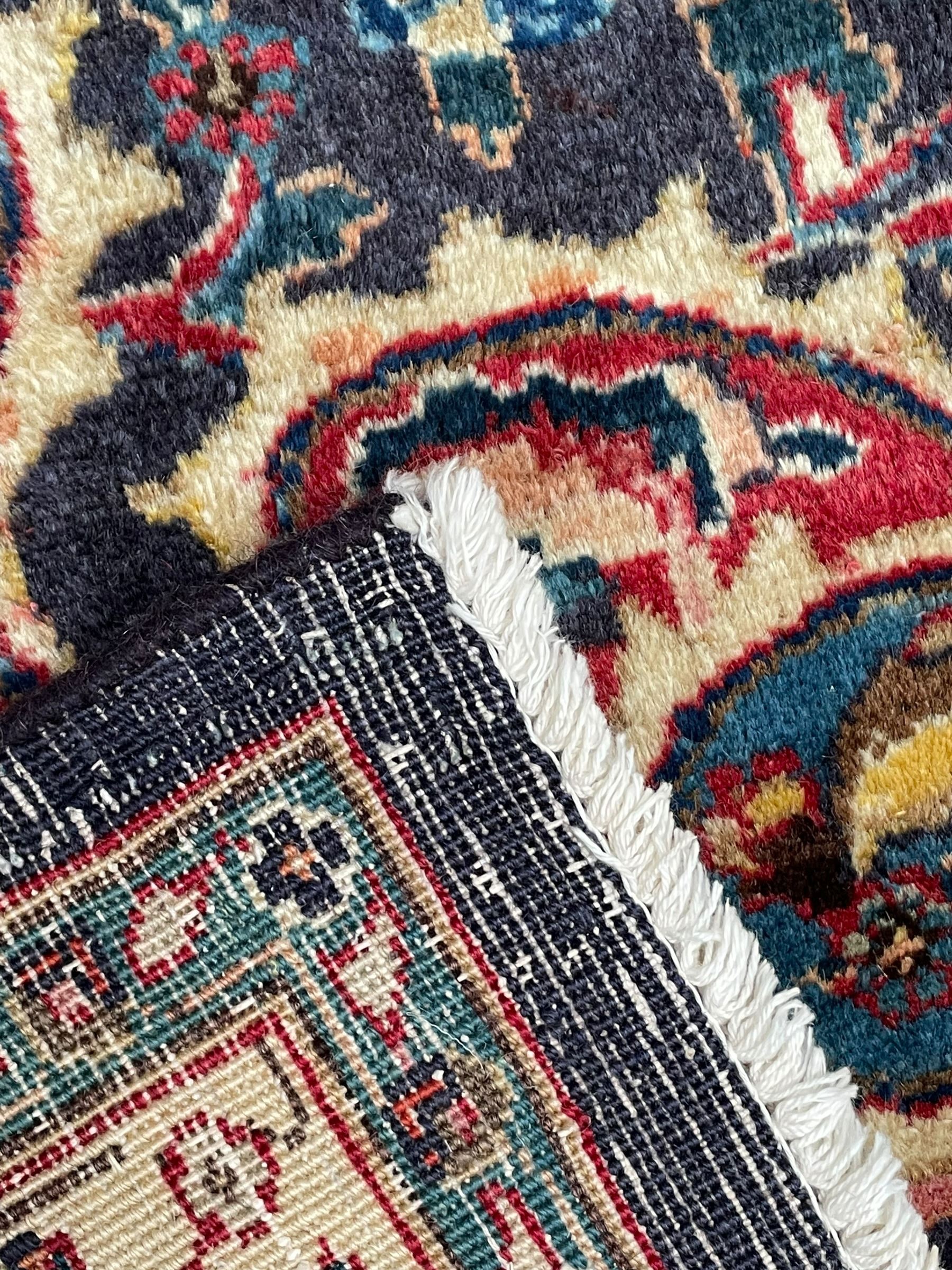 Persian Kashan indigo ground carpet, large central rosette medallion decorated with alternating palmettes, the surrounding field and spandrels with overall floral design depicting trailing branches and stylised plant motifs, crimson ground border with trailing floral pattern, enclosed within guard stripes 