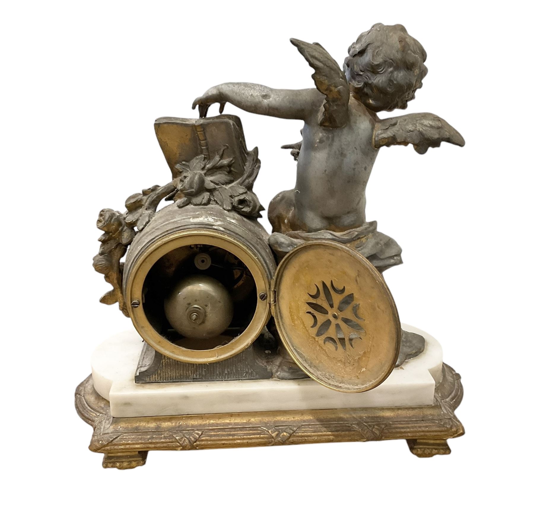 French-early 20th century 8-day patinated spelter and white marble clock garniture, with a seated winged cherub aside a drum clock movement on a white marble base supported on a gilt metal plinth with pad feet, enamel dial with Arabic numerals, minute markers and garland swags, with gilt pierced hands and a twin train countwheel striking movement, striking the hours and half hours on a bell, with a pair of conforming mounted urns.  