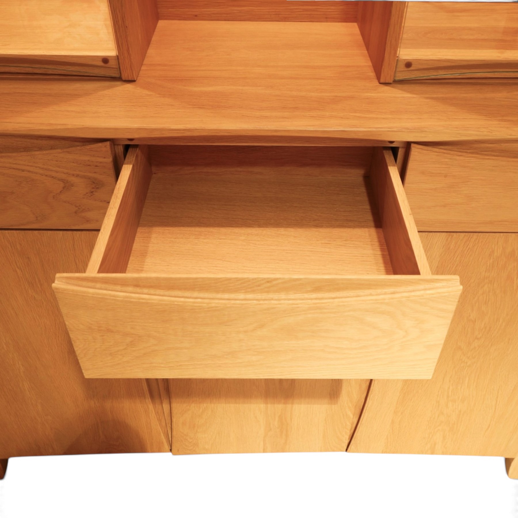 Ercol - 'Artisan' light oak dresser, upper section with cantered corners, with central open area fitted with adjustable glass shelves, flanked by twin glazed cabinets with further adjustable glass shelving, the lower section with three shorts drawers with recessed handles, above three cupboard doors with recessed handles enclosing adjustable wooden shelves, raised on short tapering supports 