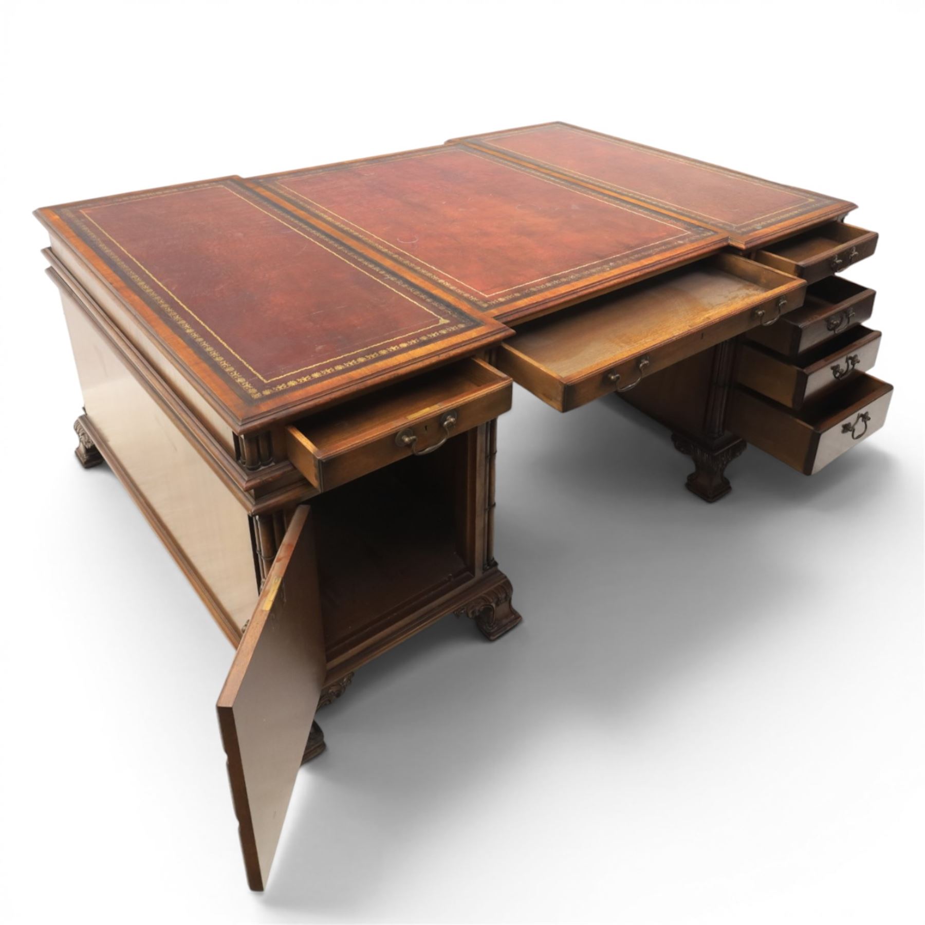 George III style large mahogany reverse breakfront partners desk, red tooled leather writing surfaces crossbanded and moulded edges, flanked by ring-turned cluster columns three frieze drawers with brass swan neck handles, raised on large pedestals with faux drawer fronted cupboard and three graduated drawers, supported on carved ogee feet decorated with C-scrolled and acanthus leaves