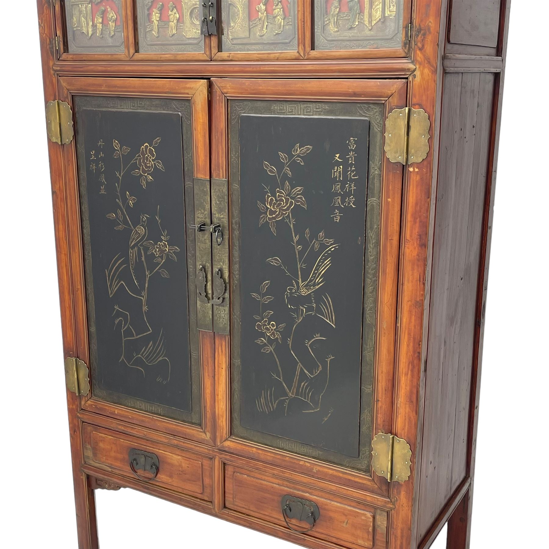 Late 19th century Chinese Qing dynasty red and black lacquered wood cabinet,  Fujianese province, upper cupboard enclosed by two doors with relief carved and gilt panels depicting figures behind glass, the large cupboard enclosed by two panelled doors carved with trailing foliate branches and birds, inscribed with Chinese characters, to the left ‘The red mountains are in the shape of Phoenixes and appear auspicious’ and to the right, ‘Wealth and honour are given by flowers and I hear the sound of the phoenix', fitted with two drawers, on square supports with carved brackets 