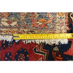 Persian Heriz crimson ground carpet, the central navy geometric medallion on a red crimson ground field, surrounded by further geometric stylised motifs and foliate designs, enclosed by multiple guard-lines  