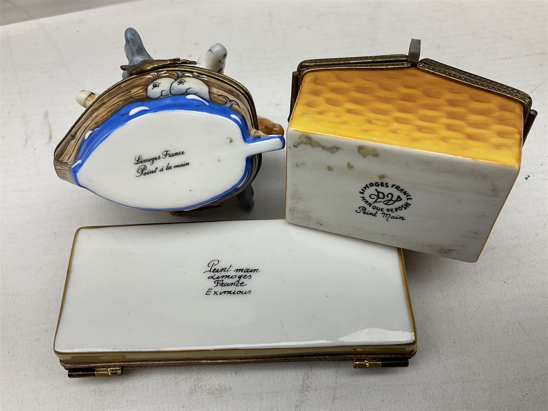 Group of Limoges trinket boxes, to include a number of novelty examples, including examples modelled as Noah's ark, shotgun case containing shotguns, picnic basket containing food, toad reading book seated upon a lily pad, etc., (9)