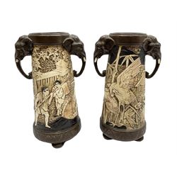 Pair of Bretby vases of tapering cylindrical form decorated with elephants, cranes and fishermen, the bodies with twin elephant mask handles, with coppered borders, raised upon three bun feet, stamped Bretby 2246 marks beneath, H32cm