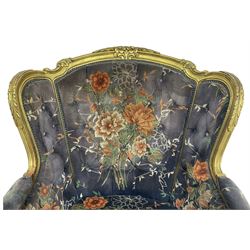 Pair of Louis XVI design gilt framed wingback armchairs, cresting rail carved and moulded with foliate decoration and C-scrolls, upholstered in buttoned floral patterned mauve velvet with loose seat cushion, scallop carved apron over cabriole supports
