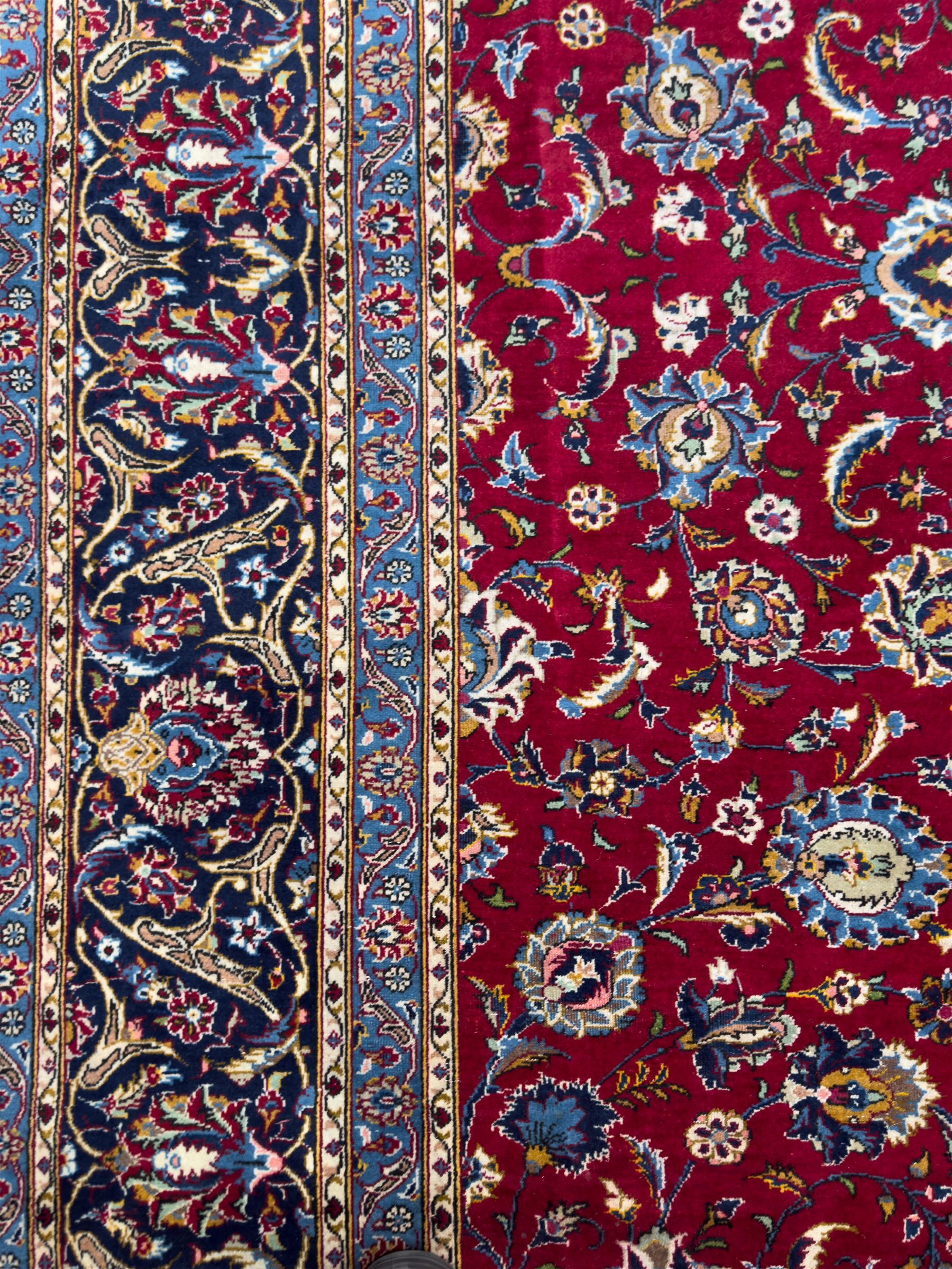Northeastern Persian Meshed hand-knotted carpet, madder red field with an all-over design of scrolling vines, palmettes, and rosettes, within a dark blue border of palmettes and arabesques 