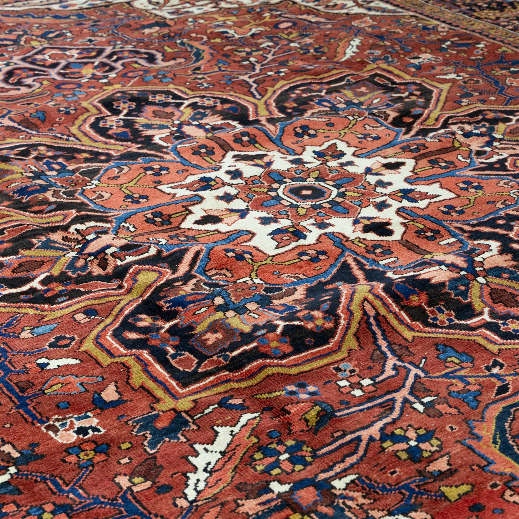 North West Persian Ahar hand-knotted carpet, madder red ground, with a large central shaped floral medallion with pendants, surrounded by angular scrolling foliate motifs incorporating rosettes, palmettes and stylised flowerheads, enclosed by ivory spandrels and a dark navy border with repeating floral motifs and meandering vines, flanked by narrow floral guard stripes, with cotton fringes