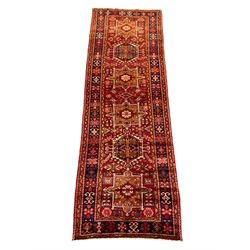 Persian Karajeh red ground runner, the field set with six trailing geometric medallions outlined in ivory, field decorated with stylised shapes, thick band with repeating pattern and multi-border