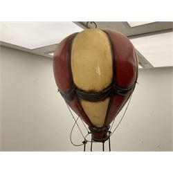 Painted wooden hanging model of a hot air balloon group, the balloon above a wicker basket complete with sandbags and figures, together with a similar example with a clown figure below, H68cm
