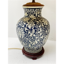 Two Oriental table lamps, each of bulbous form, the first example decorated with pink blossoming flowers upon a dark blue ground, above a fret pattern band, upon a wooden circular stepped base, the second example with white foliate decoration upon a dark blue ground, also with fret pattern band, and upon a wooden circular stepped base, each with fabric shade, including shade each approximately 74cm. 
