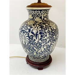 Two Oriental table lamps, each of bulbous form, the first example decorated with pink blossoming flowers upon a dark blue ground, above a fret pattern band, upon a wooden circular stepped base, the second example with white foliate decoration upon a dark blue ground, also with fret pattern band, and upon a wooden circular stepped base, each with fabric shade, including shade each approximately 74cm. 

