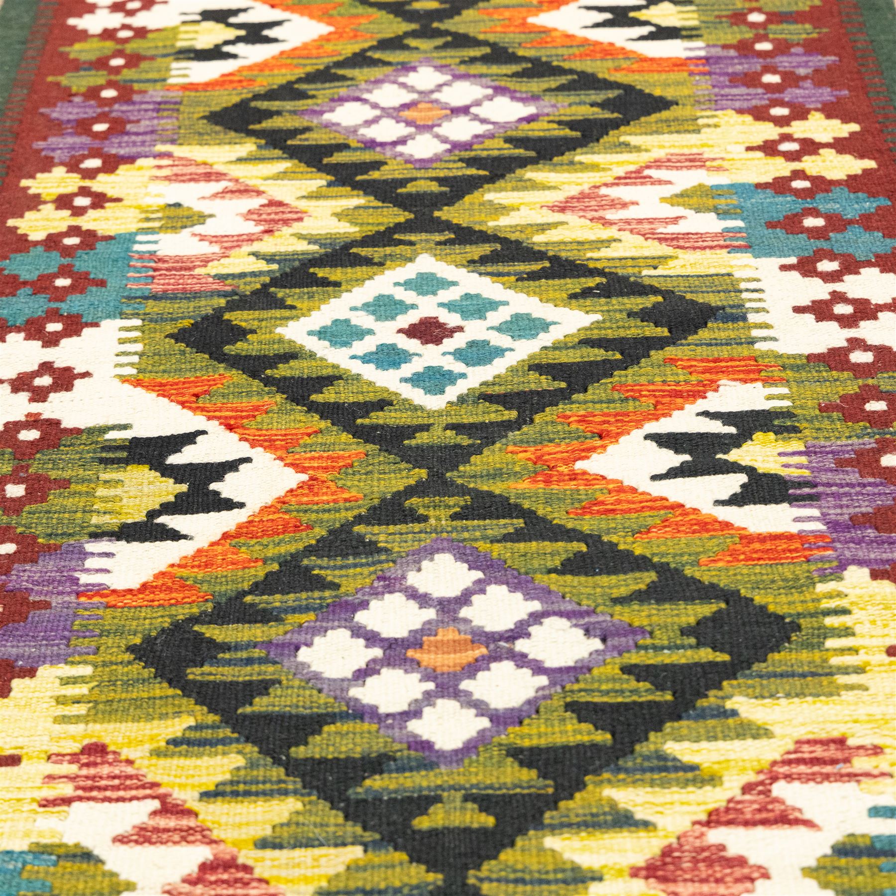 Chobi flatweave kilim runner, repeating diamond medallion design in a vibrant palette of green, red, and teal, ivory and black, within a narrow floral border