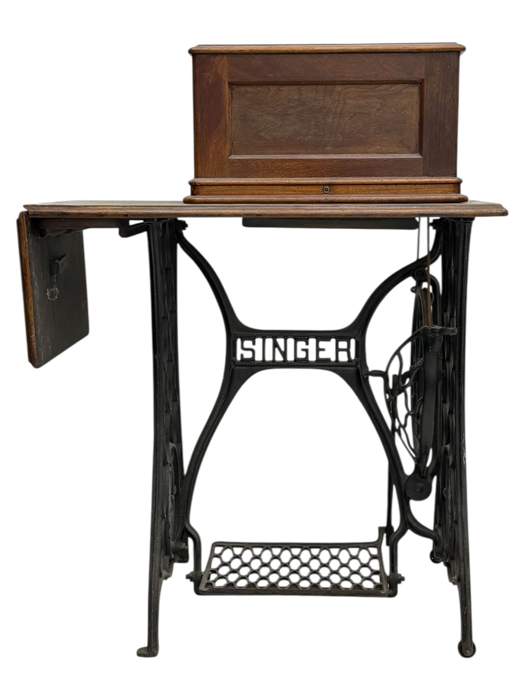 Singer - early 20th century cast iron treadle sewing machine, with hand crank wheel and oak work surface, the machine decorated with gilt foliate detail, complete with rectangular wooden cover and folding extension leaf