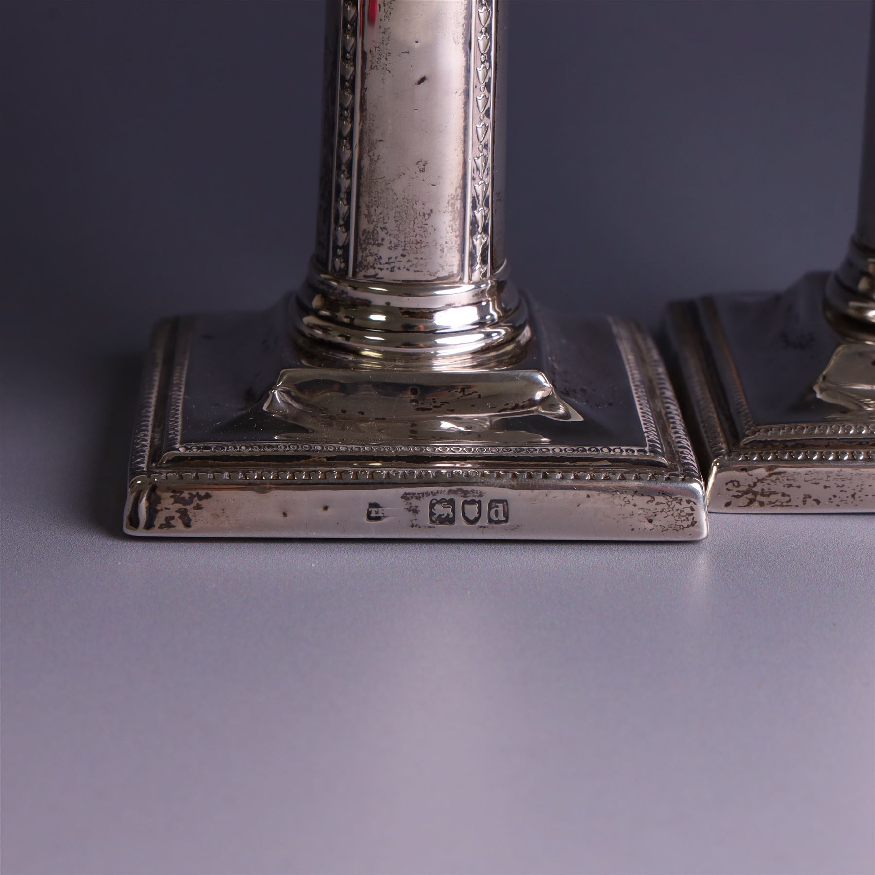 Pair of late Victorian silver mounted candlesticks, the stems embossed with classical ribbon and swag design, upon weighted stepped square bases, hallmarked London 1899, maker's mark worn and indistinct, H12cm