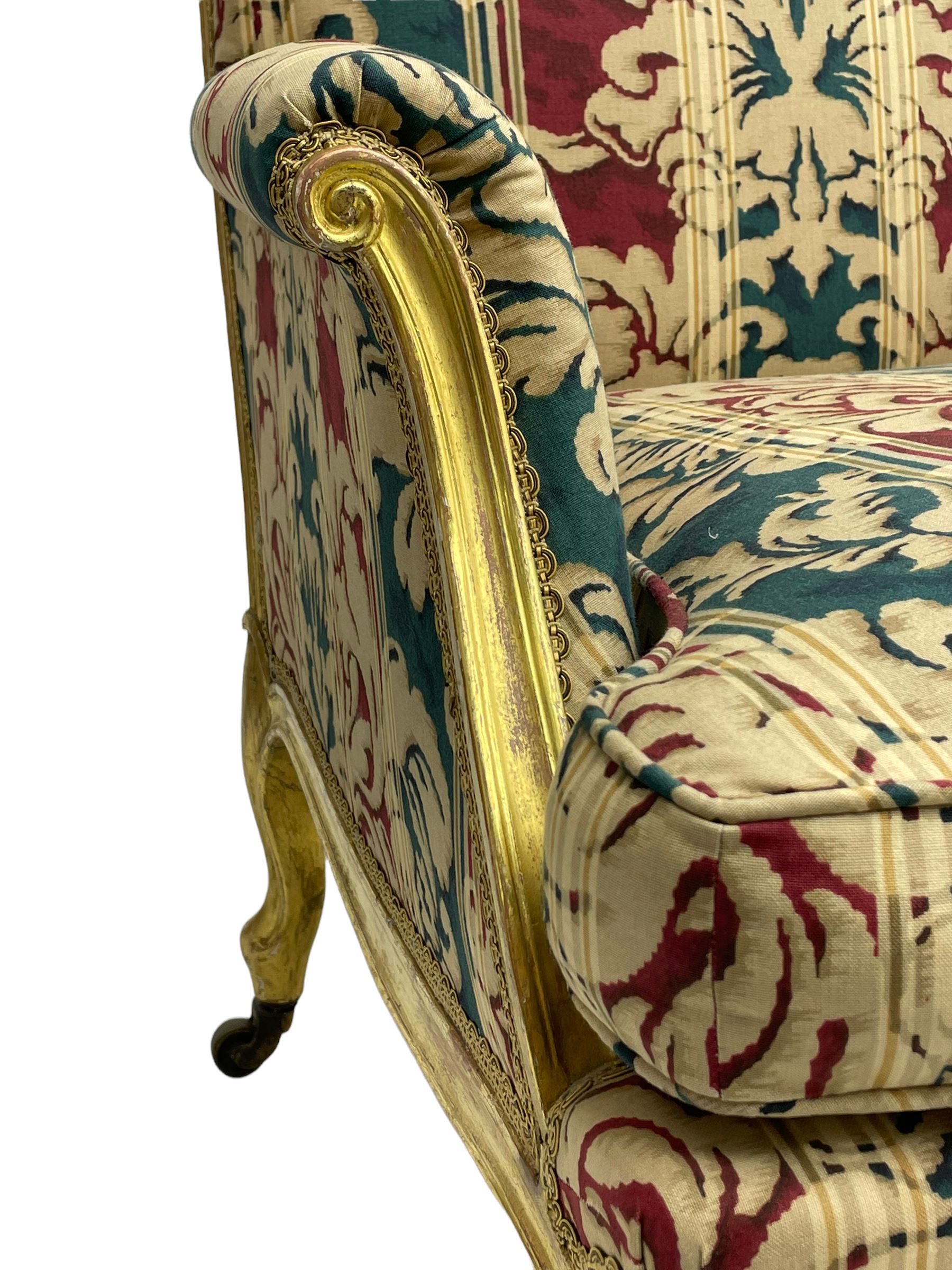William Bertram & Son of London - pair late 19th century giltwood armchairs, moulded frame with scroll carved back and arm terminals, upholstered in striped fabric with foliate pattern, on shell carved cabriole supports, the brass castors stamped 