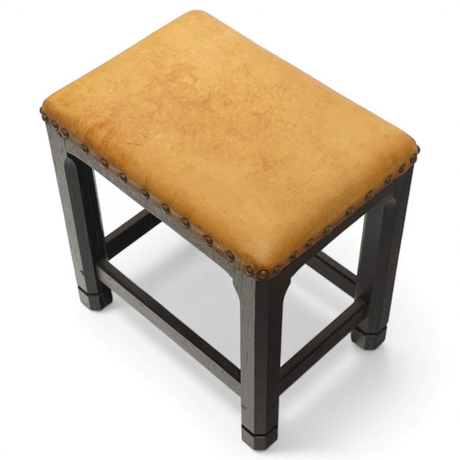 Acornman - dark stained oak stool with upholstered seat, rectangular top with tan leather seat with studded trim, raised on octagonal supports, with carved acorn signature, by the workshop of Alan Grainger of Brandsby