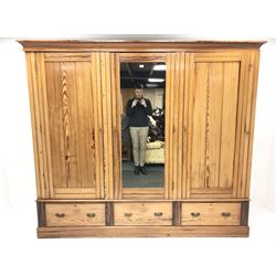 Late Victorian large pitch pine triple wardrobe, projecting cornice, central mirrored door flanked by two others above three drawers, plinth base