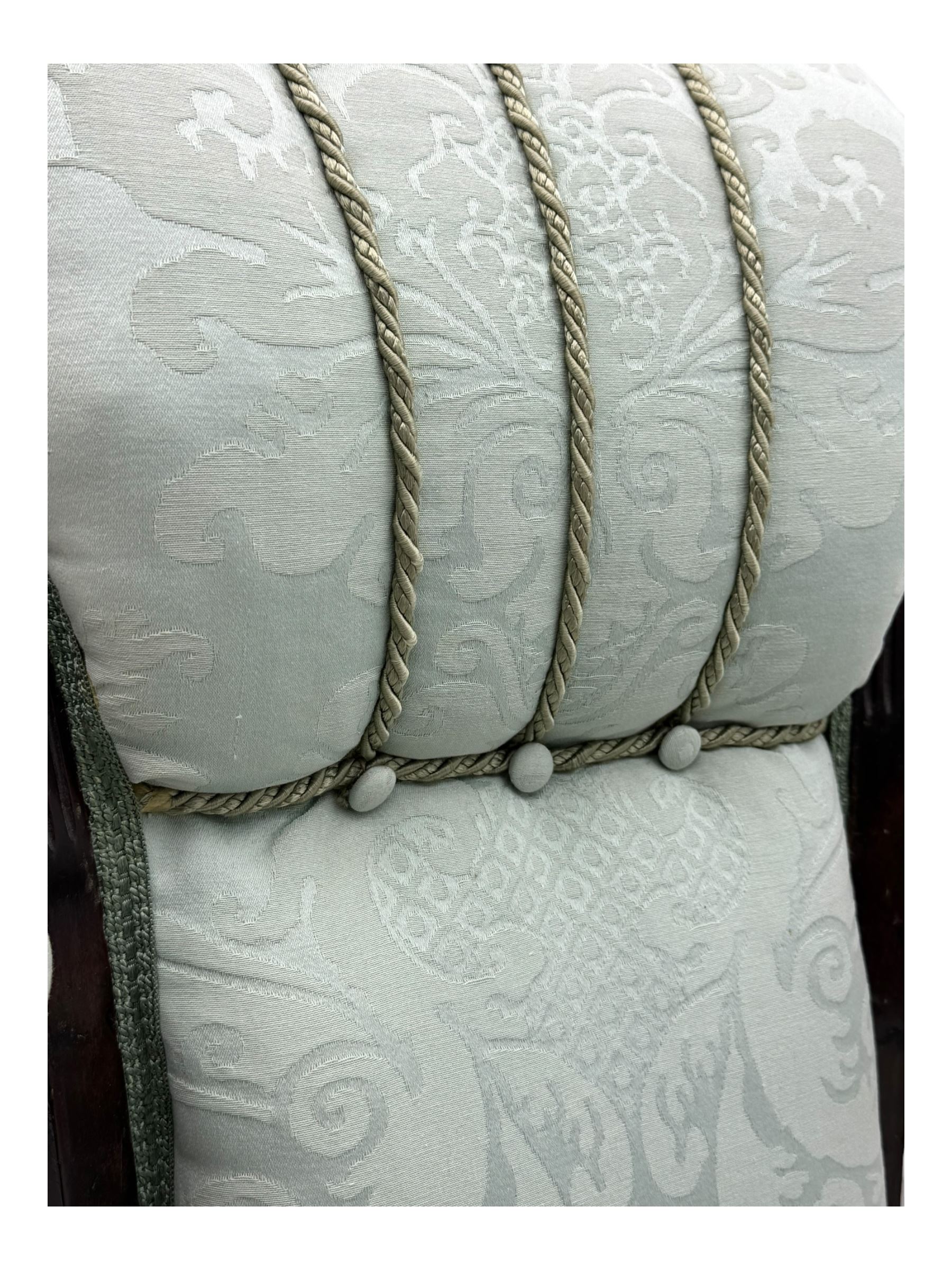 Late Victorian carved mahogany open armchair, the shaped back with fluted upholstered panel and padded arms above pierced scroll carved side supports, over a broad upholstered seat, on turned front supports