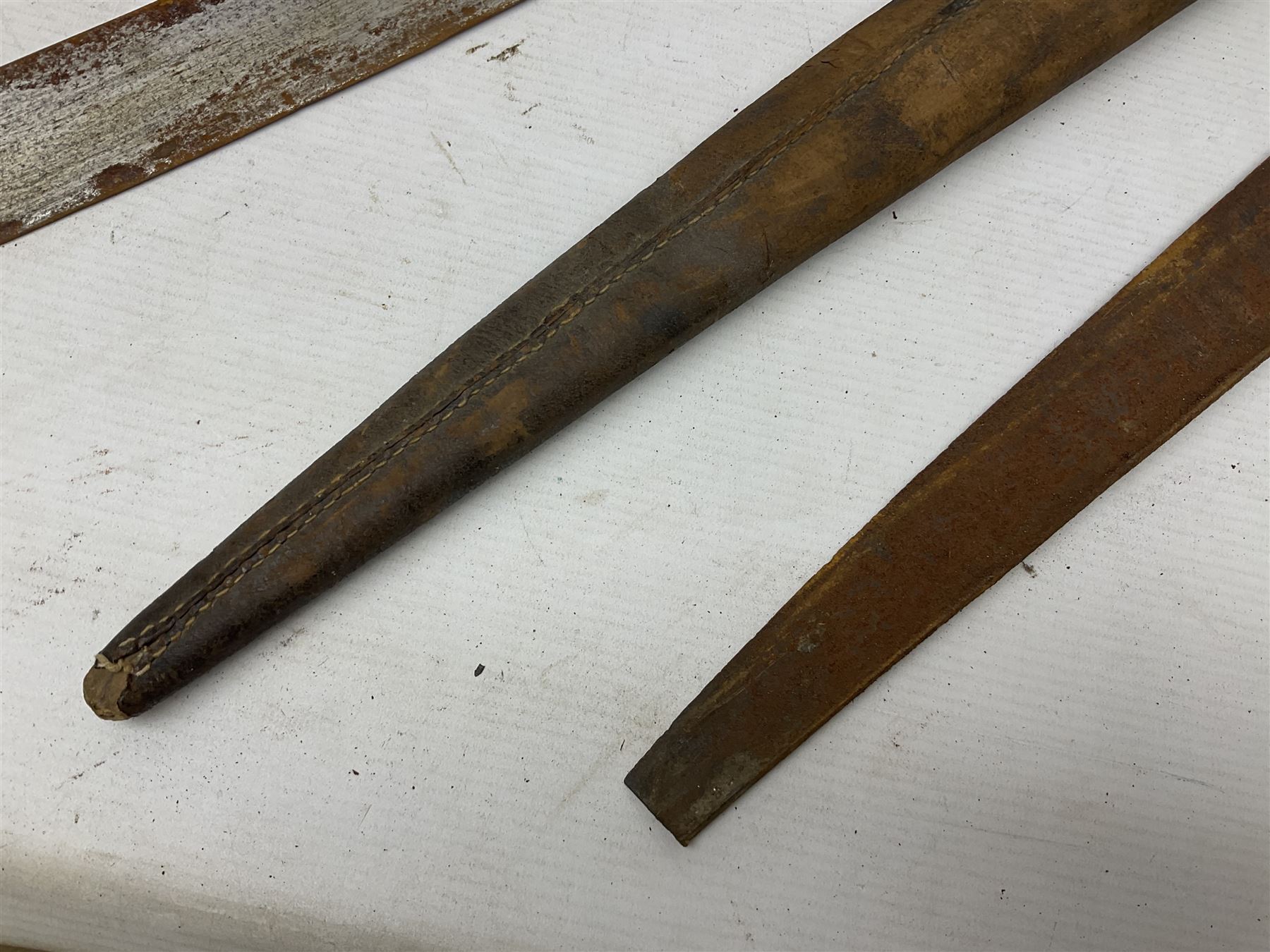 Mandingo sword, the 63cm plain curving steel blade marked with a horses head and the initials G.S.; leather covered grip with metal ribbed spherical pommel; in decorative leather leaf scabbard mounted with tassels and roundels L84cm overall; and a North African flyssa sword in poor condition with wooden scabbard (2)