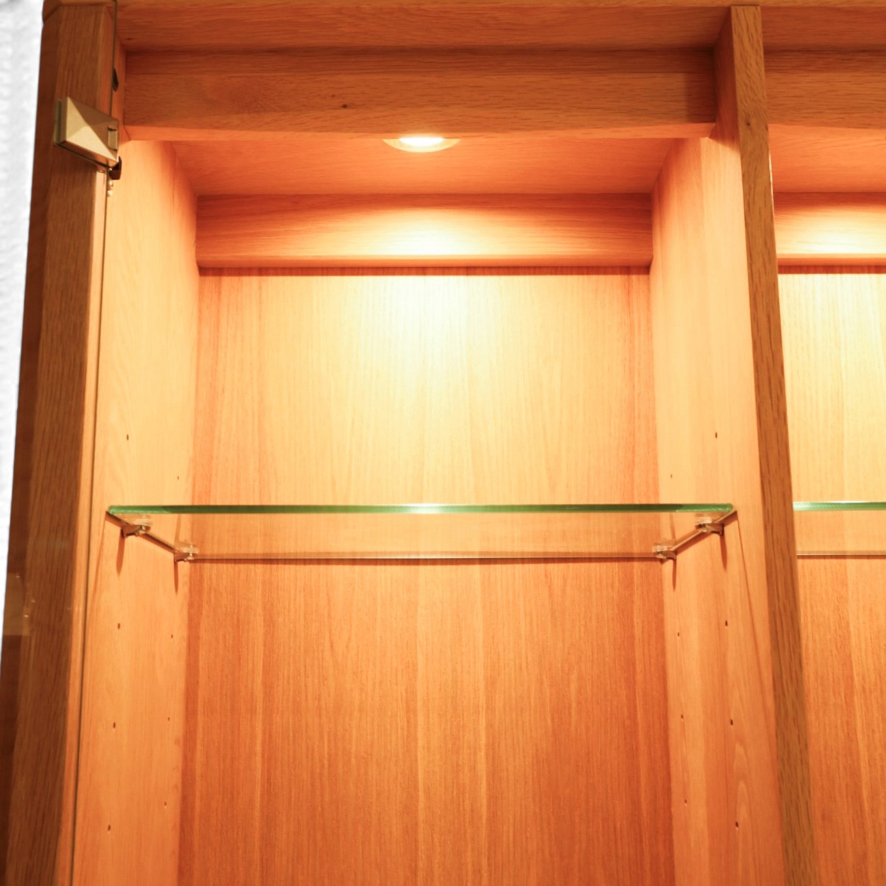 Ercol - 'Artisan' light oak dresser, upper section with cantered corners, with central open area fitted with adjustable glass shelves, flanked by twin glazed cabinets with further adjustable glass shelving, the lower section with three shorts drawers with recessed handles, above three cupboard doors with recessed handles enclosing adjustable wooden shelves, raised on short tapering supports 