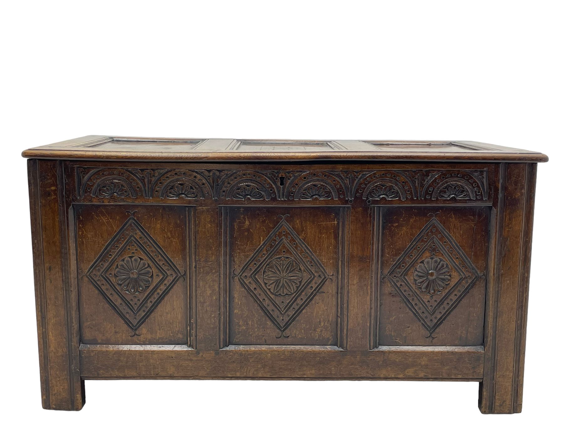 18th century oak coffer or chest, rectangular triple panelled hinged top with moulded edge enclosing main compartment and candle box, the frieze carved with repeating concentric lunettes and foliate patterns, the front fielded panels decorated with lozenges containing central flower heads, on stile supports